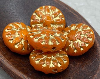 Five orange Czech coin beads with dahlia flower relief and gold wash detail, resting in a shallow wooden bowl.