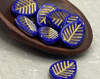 Six indigo blue Czech glass leaf beads with gold wash in a wooden dish, one separate below, showing the raised gold veining.