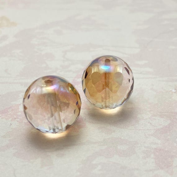 Two champagne gold Czech fire polished round beads, 18mm, faceted and iridescent on a pale background.
