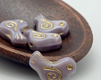 Four lilac Czech dove bird beads with gold wash detail and spiral pattern, resting in a wooden bowl against a white.