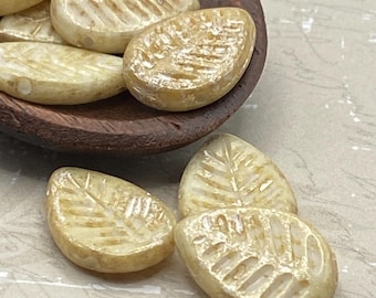 Eight yellow ivory Czech glass leaf beads with mercury finish and fine vein detail, grouped on a pale textured surface.