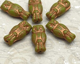 Six olive green Czech glass owl beads with copper wash detail, displayed on a wooden dish.