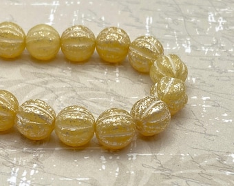 Ten yellow and ivory Czech glass melon beads with silver finish arranged in a curved line on a cream fabric background.