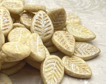 Eight yellow ivory Czech glass leaf beads with mercury finish and fine vein detail, grouped on a pale textured surface.
