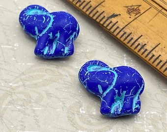 Two cobalt blue elephant beads with turquoise drip finish sitting on a dark wooden plate against a pale background.
