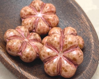 Four salmon and bronze Czech glass puffed flower beads with metallic pink thread strung through centres, resting in a dark.