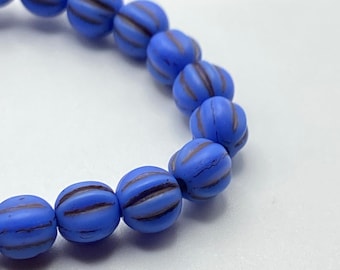 A curved line of matte indigo blue melon beads with brown wash and ridged texture on a neutral background.