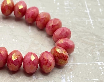 Eight pink Czech glass rondelle beads with golden Picasso finish arranged on a pale textured background.