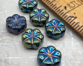 Six black iris rainbow AB puffed daisy Czech flower beads arranged on a pale background next to a wooden ruler for scale.