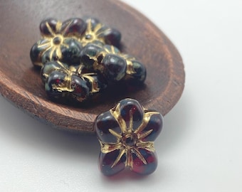 Five deep burgundy Czech glass puffed flower beads with gold wash detailing, displayed on a rustic brown wooden dish against.