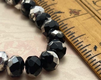 Black and silver faceted Czech glass rondelle beads in a wooden bowl, approximately fifteen beads visible