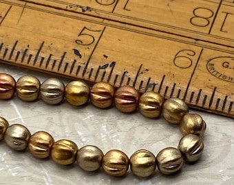 Around 25 matte metallic Czech glass melon beads in bronze and gold tones displayed next to a wooden ruler for scale.