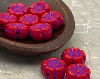 Red Czech glass hibiscus flower beads with violet wash arranged in a wooden bowl and on a pale surface.
