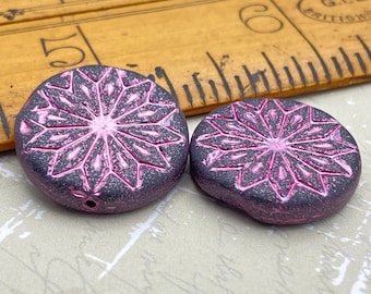 Two deep purple origami flower coin beads with metallic pink embossed petals, shown next to a wooden ruler for scale.