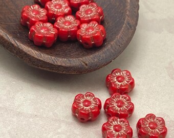 Czech Hawaii flower beads in bright red with copper wash detail, displayed in a wooden dish and on a pale surface.