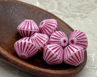 Eight Czech glass bicone lantern beads in chalk pink with metallic tribal stripes displayed on a wooden dish.