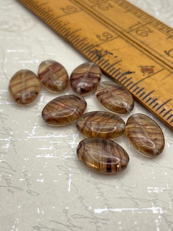 Eight brown maroon bronze marble Czech glass oval beads shown next to a wooden ruler for scale.