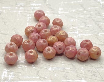Twenty-five pale pink Picasso round beads with textured gold finish arranged on a neutral patterned background.
