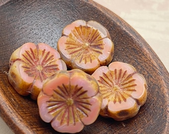 Four pink Czech glass hibiscus flower beads with golden details in a wooden bowl.