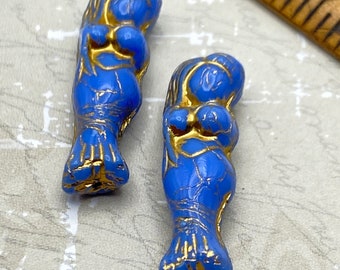 Two Czech glass mermaid beads in periwinkle blue with gold wash detail, shown with a ruler for scale.