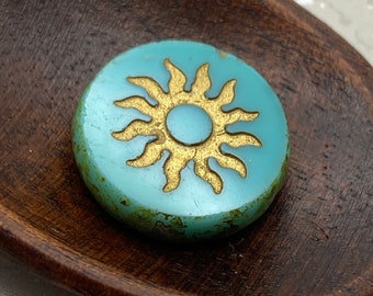 Czech glass sun coin bead in turquoise with gold-washed sun detail, resting on a wooden dish.