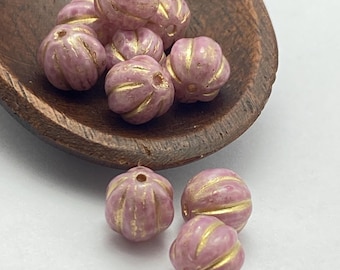 Czech glass melon beads in mauve-pink with gold wash details, arranged in a wooden dish and scattered on white surface.