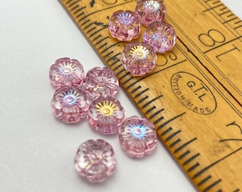 Czech glass hibiscus flower beads in pink crystal with iridescent centres, shown in a wooden spoon and scattered on white.