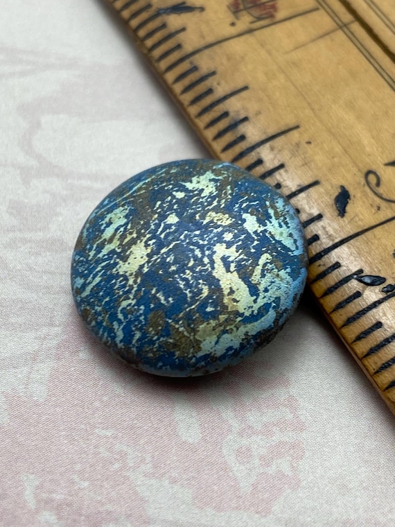 One blue-green laser etched planet earth glass coin bead next to a wooden ruler for scale.