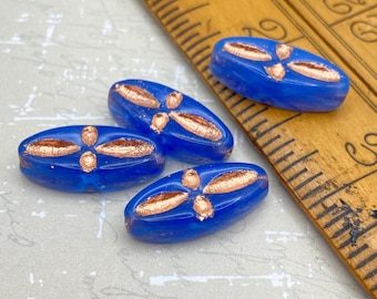 Four hyacinth blue marquise beads with copper wash decoration, displayed beside a wooden ruler for scale.