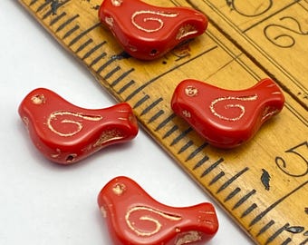 Three red Czech dove bird beads with copper wash and white detailing, positioned next to a wooden ruler for scale.