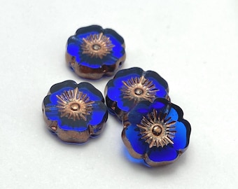 Four Czech table cut hibiscus flower beads in sapphire blue with bronze finish centres on a plain white background.