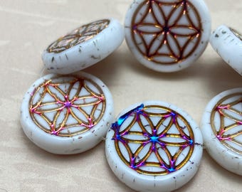 Czech glass flower of life mandala beads with white base, geometric pattern and rainbow metallic wash, on plain background.