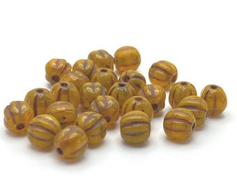 Twenty-five golden yellow Czech glass melon beads with dark striped detail on a wooden dish.