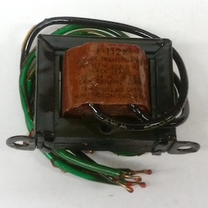 May include: A black and brown transformer with green and black wires. The transformer has the text "F-112X TRANSPO 50/60 HZ BLACK LEADS SEC VOLTS 25 12 AMP-UTRAD DIST HUNTINGTON, IND. USA" printed on it.