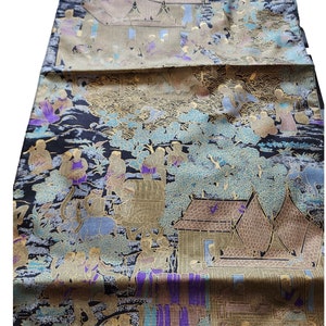 May include: A black fabric with a gold and silver design depicting a scene of people and buildings. The fabric has a textured surface and a traditional Asian style.
