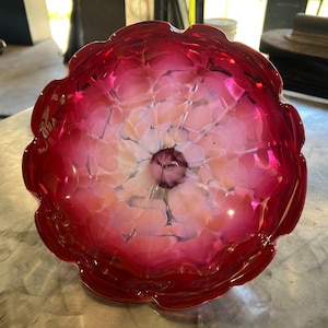 May include: A large, red glass bowl with a white and pink marbled design. The bowl has a scalloped edge and a deep, round shape.