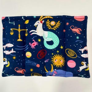 May include: A rectangular, navy blue fabric item featuring a celestial zodiac design. The design includes illustrations of zodiac symbols, planets, stars, and a sun with a smiling face. The edges are finished with a pink border.