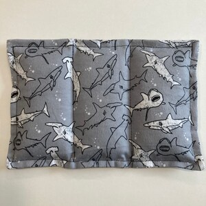 May include: A gray fabric rectangular pillow with a white shark pattern. The pillow is sewn together with a white thread. The pillow is filled with a soft material.