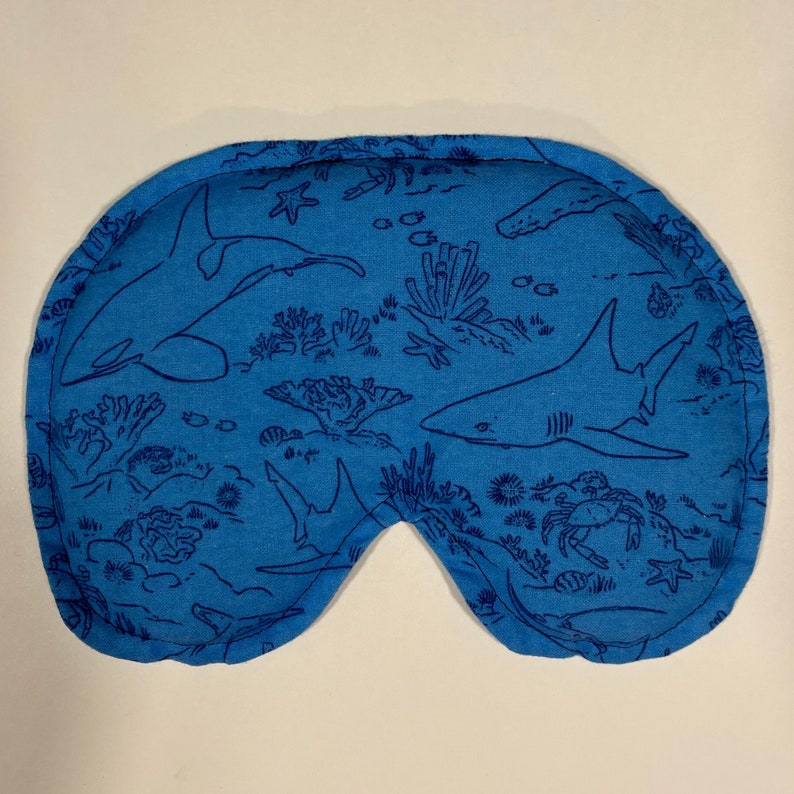 Puede incluir: M&aacute;scara de dormir azul con un patr&oacute;n de tibur&oacute;n y arrecife de coral.