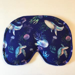 Puede incluir: Una m&aacute;scara para dormir azul con un patr&oacute;n de vida marina. El patr&oacute;n incluye ballenas, tortugas marinas, medusas y algas marinas.