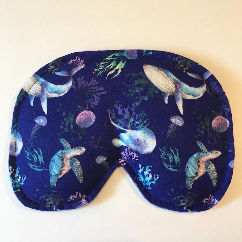 Puede incluir: Una m&aacute;scara para dormir azul con un patr&oacute;n de vida marina. El patr&oacute;n incluye ballenas, tortugas marinas, medusas y algas marinas.