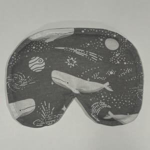 Puede incluir: Una m&aacute;scara para dormir gris con un patr&oacute;n de ballena blanca y estrellas. La m&aacute;scara est&aacute; hecha de tela suave y est&aacute; dise&ntilde;ada para bloquear la luz.