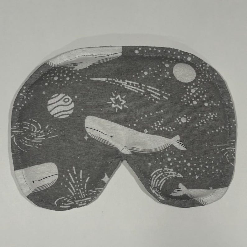 Puede incluir: Una m&aacute;scara para dormir gris con un patr&oacute;n de ballena blanca y estrellas. La m&aacute;scara est&aacute; hecha de tela suave y est&aacute; dise&ntilde;ada para bloquear la luz.
