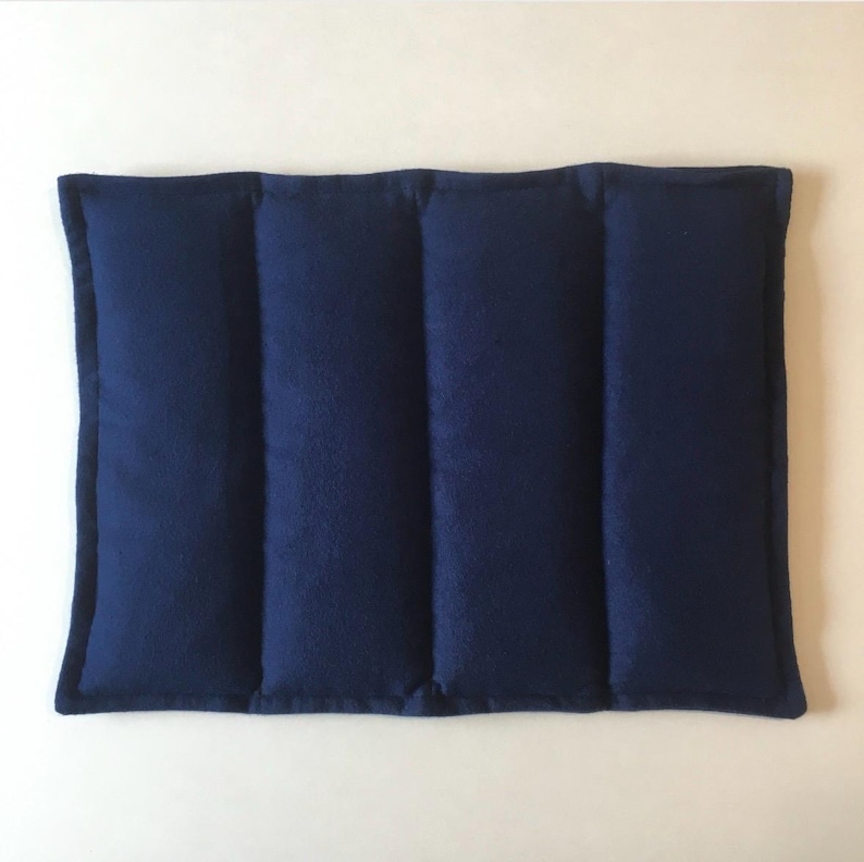 May include: A navy blue rectangular heating pad with three sewn-in compartments. The pad is made of a soft, plush fabric.