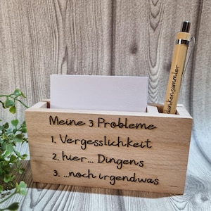 Könnte beinhalten: Ein hölzerner Schreibtisch-Organizer mit drei Fächern. Der Organizer hat den Text "Meine 3 Probleme" und eine Liste mit drei Punkten: "1. Vergesslichkeit", "2. hier... Dingens", und "3...noch irgendwas". Ein Stift mit dem Text "danken sammler" befindet sich im oberen Fach.