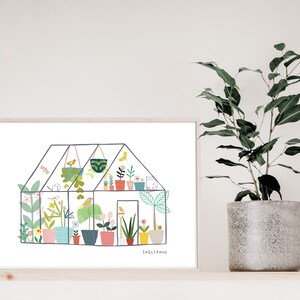 May include: A colourful illustration of a greenhouse filled with plants and flowers. The illustration is in a white frame and is on a wooden shelf with a potted plant.