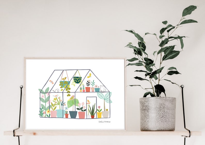 May include: A colourful illustration of a greenhouse filled with plants and flowers. The illustration is in a white frame and is on a wooden shelf with a potted plant.