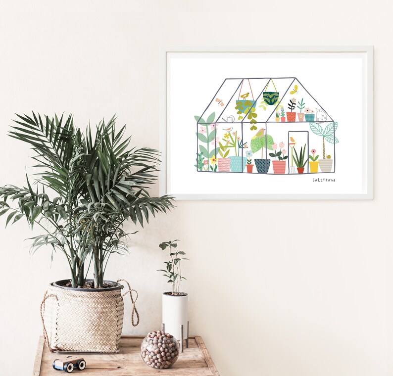 May include: A white framed print of a colourful illustration of a greenhouse filled with plants and flowers. The text "Sally Paine" is at the bottom of the print.
