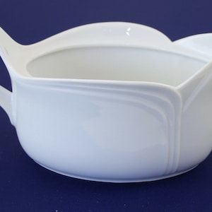 Puede incluir: Salsera de porcelana blanca con asa curva y borde festoneado.