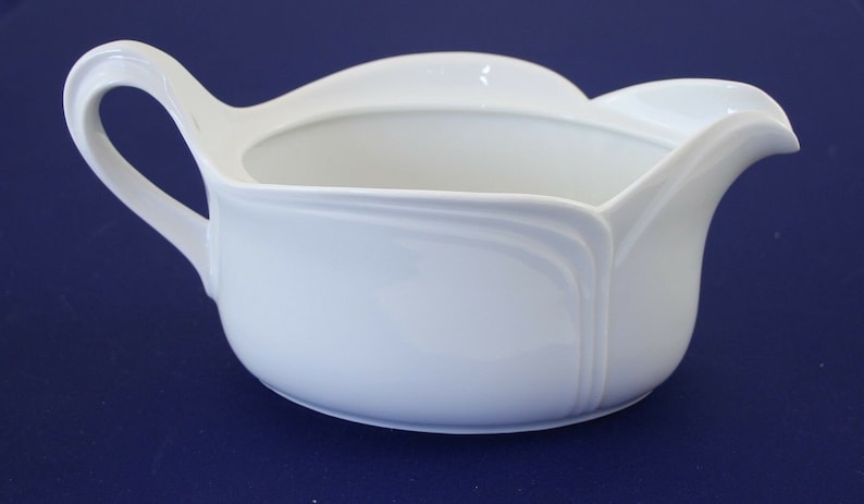 Puede incluir: Salsera de porcelana blanca con asa curva y borde festoneado.